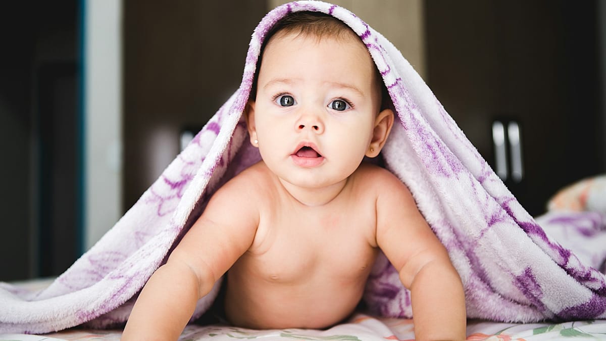 Bebé asomando bajo una manta sobre la cama a la hora de dormir