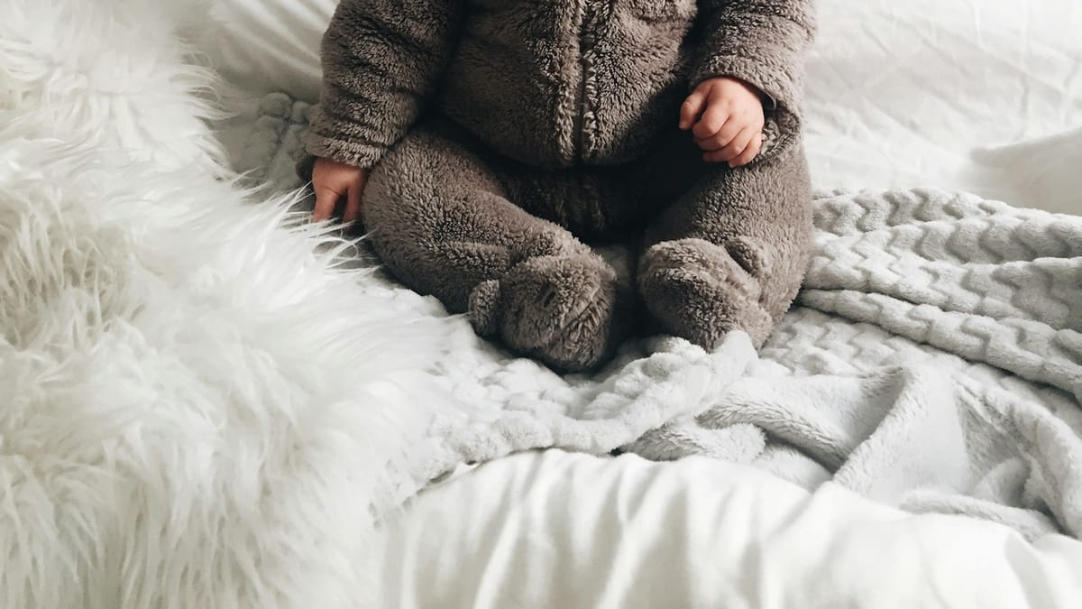 Bebé con pijama de osito sentado sobre una cama