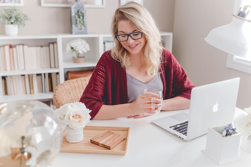 Mujer sonriendo con una taza de té frente a su laptop durante una sesión online
